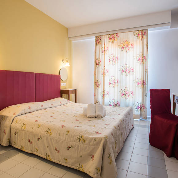 Nami Hotel Suites Family Room bedroom with decorated double bed, table with a chair and amenities